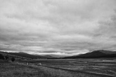 A train track cuts across the valley with distant hills, North-west Scotland
